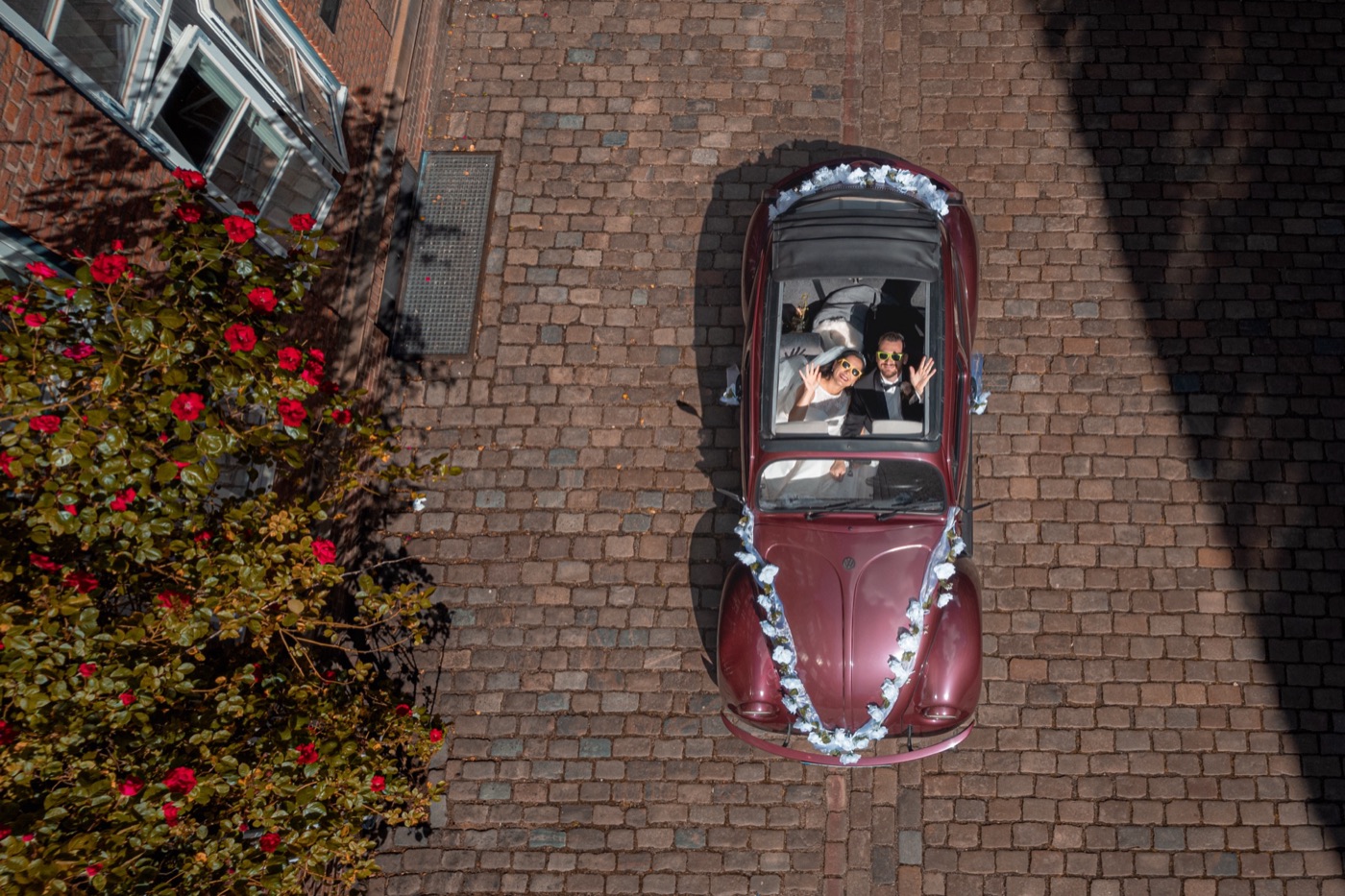 Hochzeitsauto von oben – Brautpaar winkt aus dem Cabrio